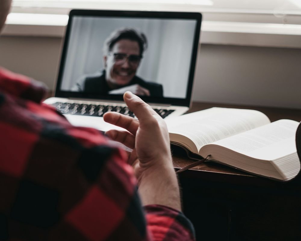 Sesión de estrategia online: una persona habla por videollamada con su asesor, con un libro abierto sobre la mesa